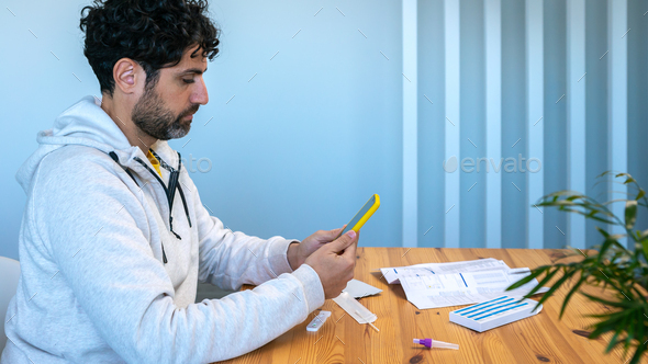 Man using smartphone after make antigen diagnostic test Covid-19 device at home