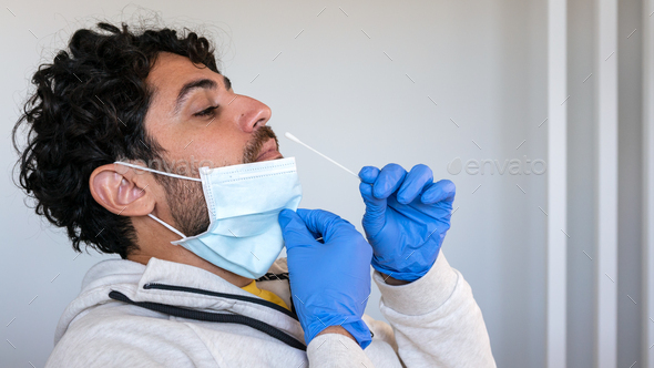 A man wearing mask and latex gloves inserts a cotton swab into a nose to COVID19