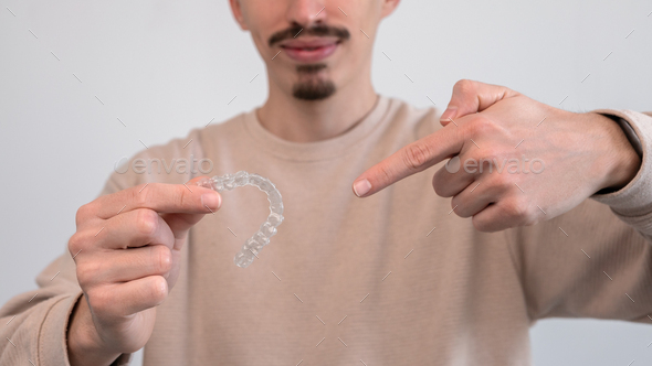 Adult man pointing hand to dental aligner retainer for beautiful teeth treatment