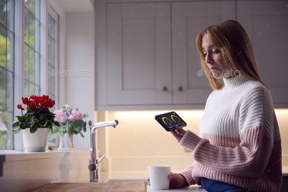 Worried Woman Looking At Smart Meter In Kitchen At Home During Cost Of Living Energy Crisis