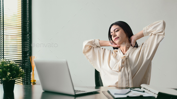 Shot of beautiful female employee relaxing at work, reclining back in chair and stretching her arms.