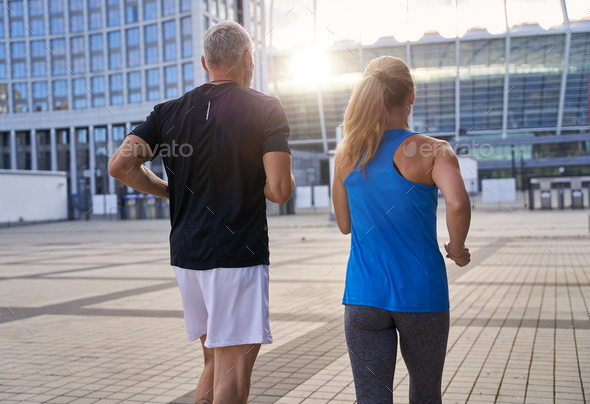 Back view of sporty middle aged couple staying active, running together in urban environment