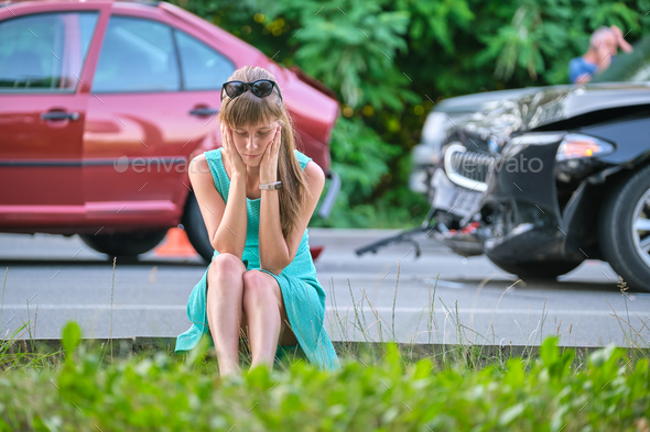 Stressed woman driver sitting on street side shocked after car accident.