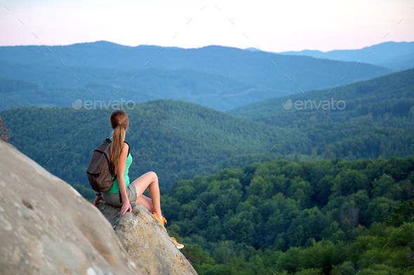 Tired hiker girl relaxing on rocky mountain top enjoying evening nature