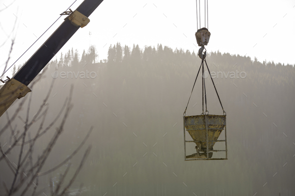 Bucket container with liquid concrete hanging on crane hook on copy space background.