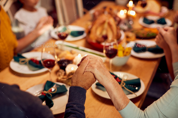 Close-up of senior couple holding hands with their family while praying on Thanksgiving dinner.