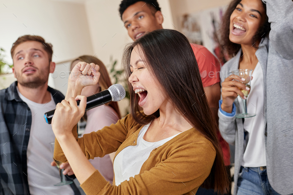 Perform like a superstar. Pretty young asian girl holding microphone ...