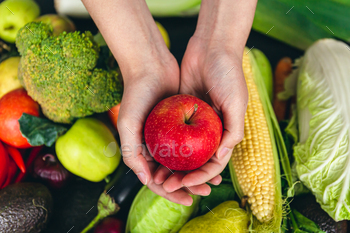 Close-up, an apple in a female hand on a blurred background with vegetables.