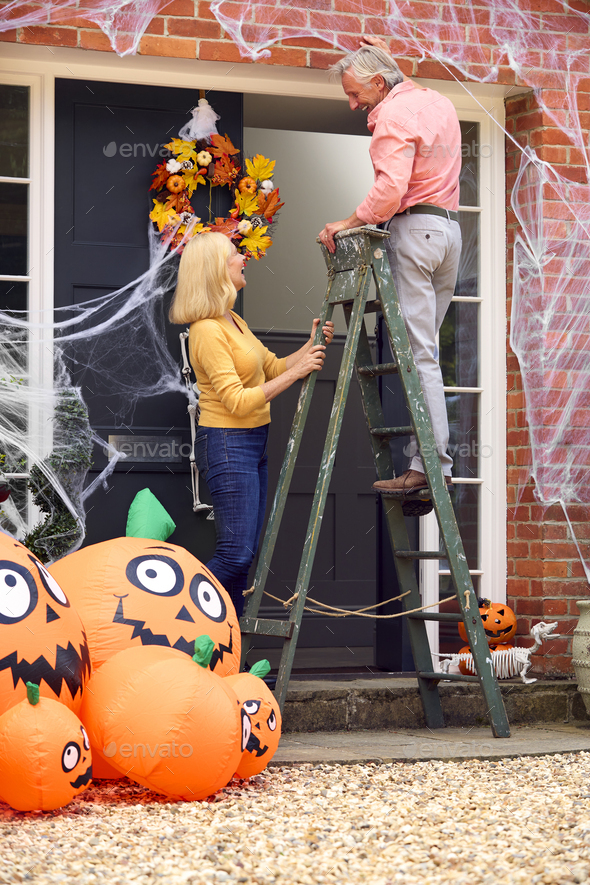 Grandparents At Home Putting Up Halloween Decorations For Trick Or