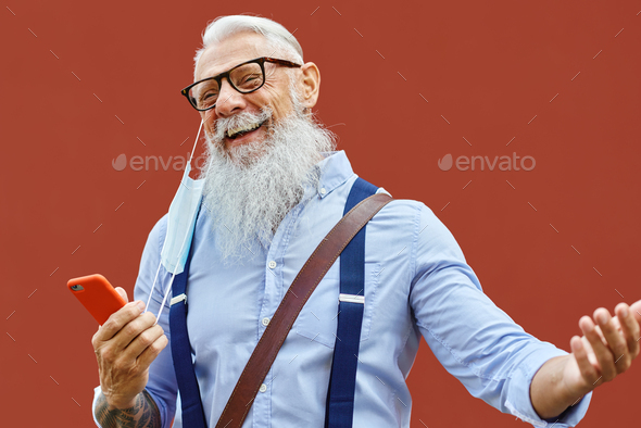 Happy Caucasian hipster man with mobile phone takes off mask at end of pandemic in background.