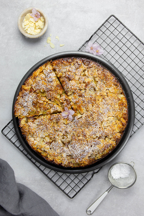 Almond homemade cake with sliced almonds crust and icing powder sugar on gray concrete background.