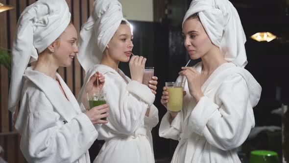 Caucasian Women Relaxing and Drinking Juicy Beverage Smoothies in Robes During Wellness Weekend