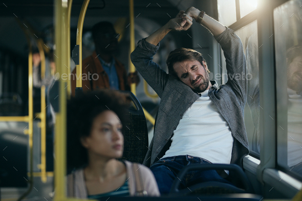 Exhausted man stretching while traveling by bus.