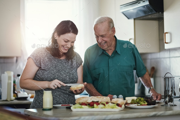 Its an honor to care for aging parents. Shot of a woman making her senior parent a sandwich.