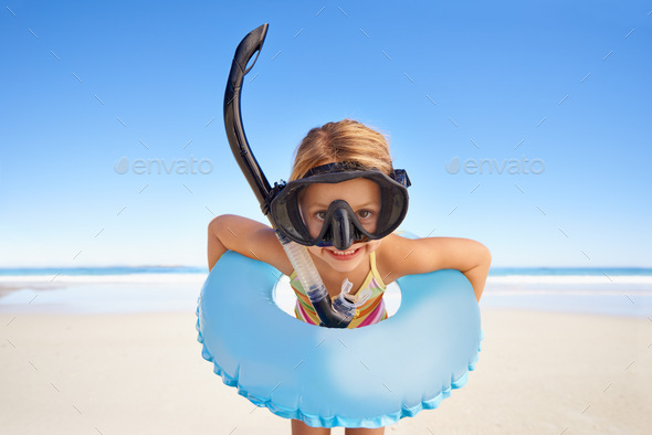 Portrait of an excited little girl standing on the beach with all her swimming gear