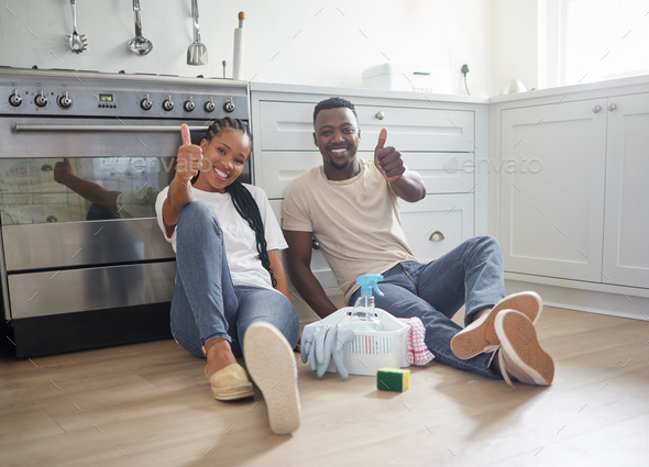 We got the job done. Shot of a young couple showing a thumbs up after cleaning up at home.