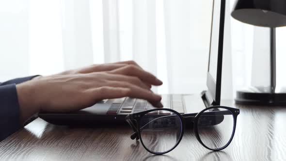 A Man Working with a Laptop on a Desktop Next to a Window alt