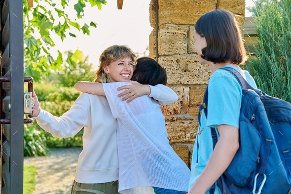 Meeting of friends, young female with guy and girl joyfully hugging near front door
