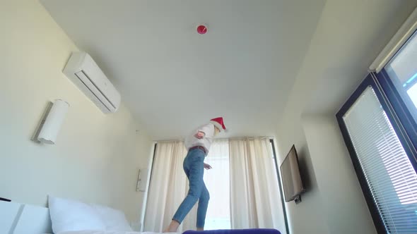 slender beautiful girl dancing in a Santa Claus hat on the bed. alt