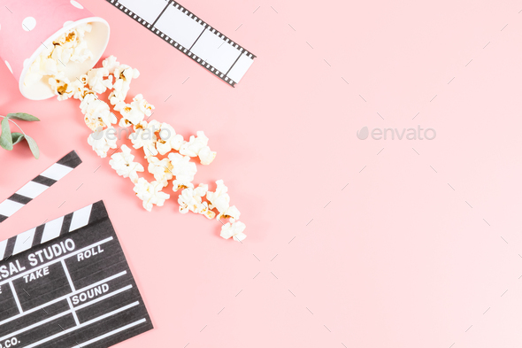 Movie clapperboard, movie tape and paper cup with sprinkled popcorn on a pink