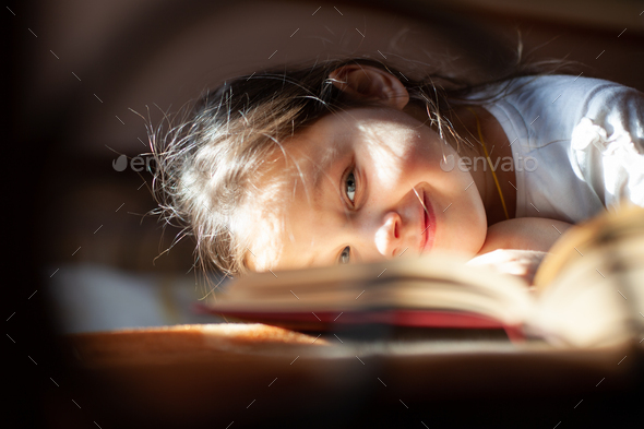 close-up portrait through the bars of a cast-iron bed of a smiling girl lying face down on an open