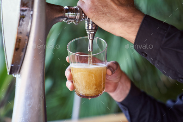 an unrecognizable person filling a glass of cold beer on tap