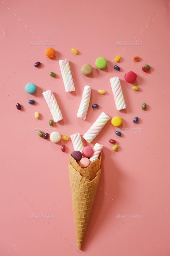 Ice cream cone with marshmallows and colorful candy on pink background. Stock Photo by