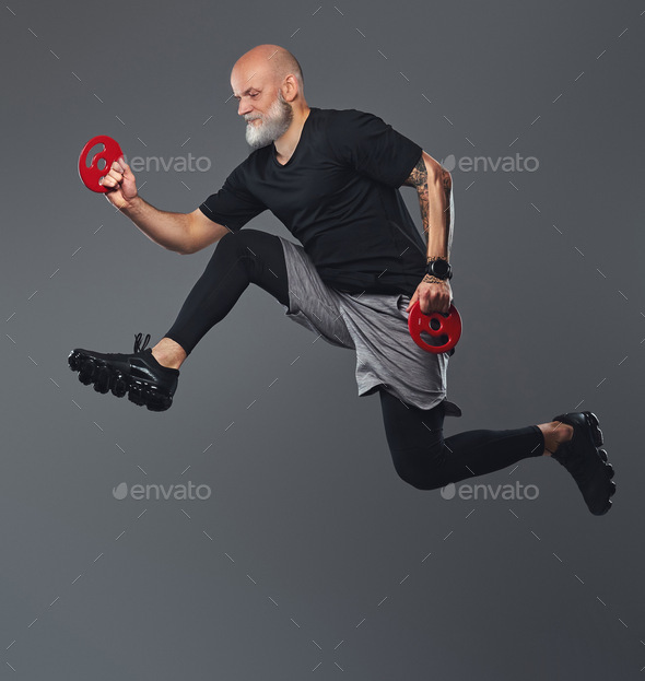 Jumping elderly man holding fitness disks against grey background - Stock Photo - Images