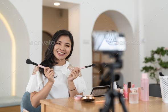 Asian female beauty blogger live streaming to review makeup product on social media, Modern young