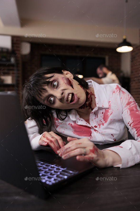 Scary horrific zombie using laptop at desk