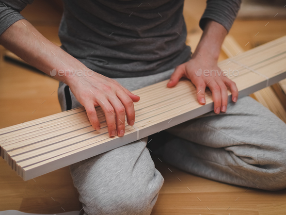 A caucasian young man counts white wooden slats for a bed base