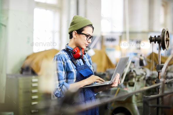 Girl in workwear using laptop in factory shop