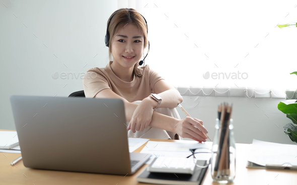 Asian businesswoman talking to colleague team in video call conference writing note on book with