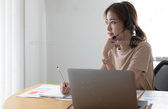 Asian businesswoman talking to colleague team in video call conference writing note on book with