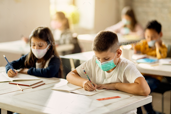 Elementary students with protective face mask back at school after coronavirus epidemic.