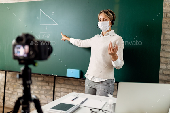 Female teacher with a face mask giving online math lecture during coronavirus epidemic.