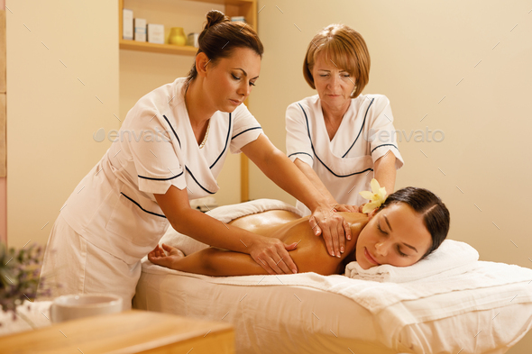 Relaxed woman receiving back massage by two therapists at health spa.