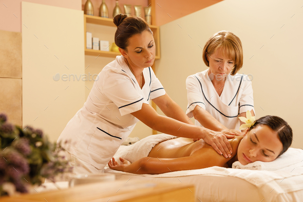 Two massage therapists massaging back of a young woman at the spa.
