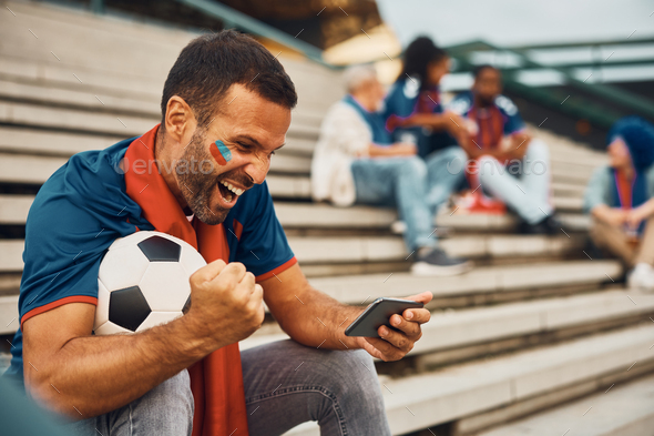 Passionate soccer fan cheering while watching a match on mobile phone.