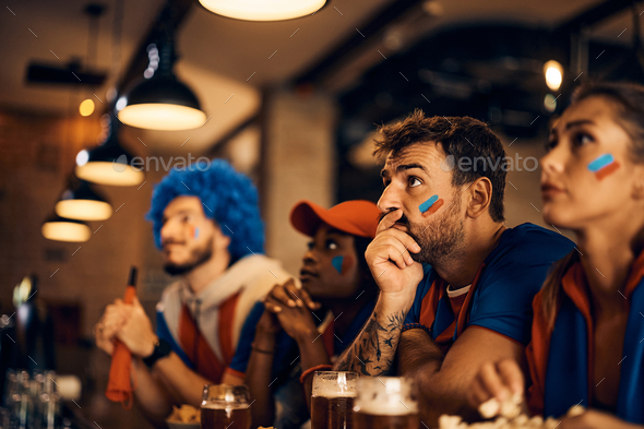 Sports fan and his friends watching football match on TV during the world cup in a bar.