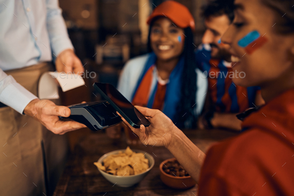 Close up of sports fan paying with her cell phone during the world cup in bar.