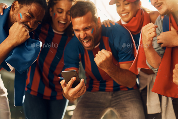 Excited soccer fans celebrating winning goal of favorite team while watching match on smart phone.