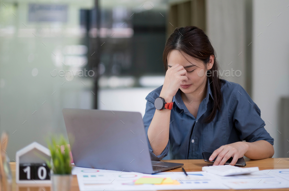 Asian women sitting in a home office With stress and eye strain.Tired businesswoman holding