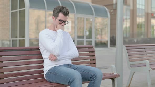 Tired Young Man Sleeping While Sitting Outdoor on Bench alt