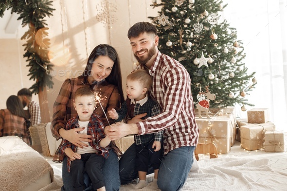 Young family in plaid shirts sitting near Christmas tree with a sparkler