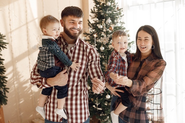 Young family in plaid shirts standing near Christmas tree with a sparklers