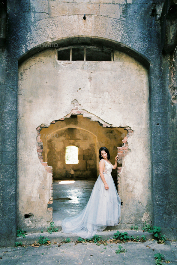 Bride stands near the dilapidated entrance of the old fortress