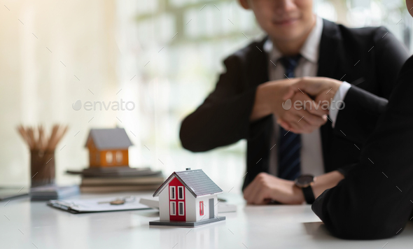 Estate agent shaking hands with his customer after contract signature, Contract document and house
