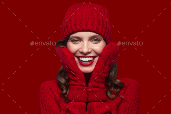 Portrait of woman wearing christmas warm knitted mittens and hat on red background