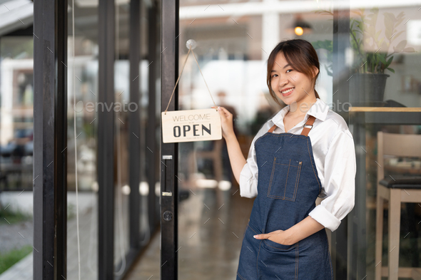 Young Asia manager girl changing a sign from closed to open sign on door cafe looking outside